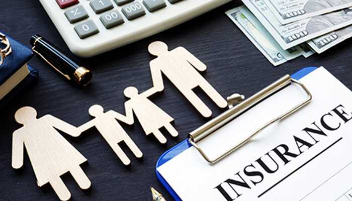 A table with an insurance pad, calculator, money, pen cap, book, and wooden cutouts of a family represents group life insurance.