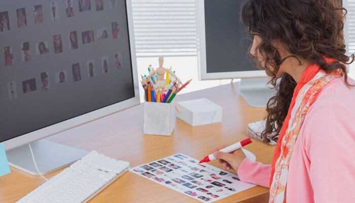 A designer working at a desk looking over some sticker designs on paper and computer; focusing on choosing the custom sticker size.