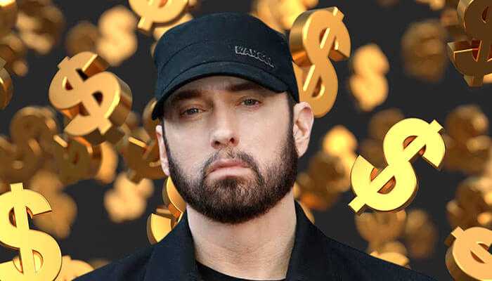 Eminem striking a serious look in a black cap and jacket with floating gold dollar signs to show eminem net worth.