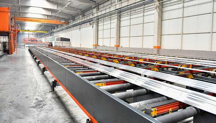 A manufacturing facility showcasing a profile extrusion line with long metal profiles on conveyor belts, illustrating the precision and efficiency of the extrusion process in modern manufacturing