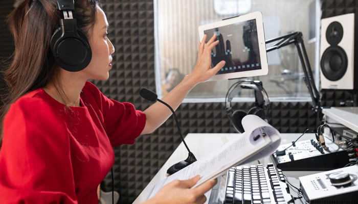 The radio broadcaster with online radio software on the tablet and speaking into a microphone in a studio.