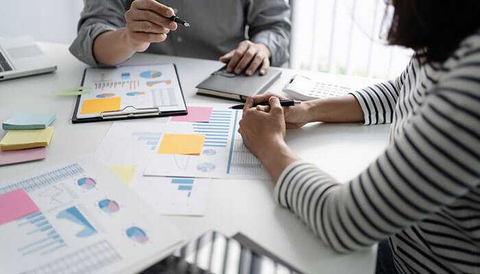 Two people discussing charts and data on a table, representing the planning and analytics involved in loan referral programs for affiliate marketers