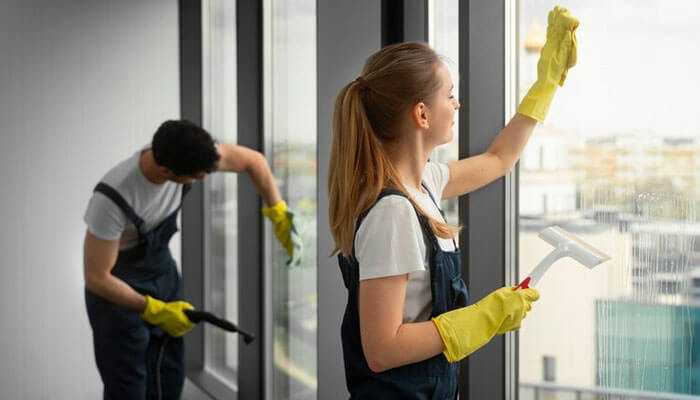 Professional cleaners performing end-of-lease cleaning as part of a moving out routine, focusing on window cleaning in a rental property