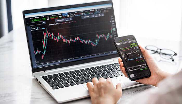 An image of a person using a laptop and smartphone to monitor cfd trading charts, highlighting real-time market data and trends in cfd trading vs financial spread betting