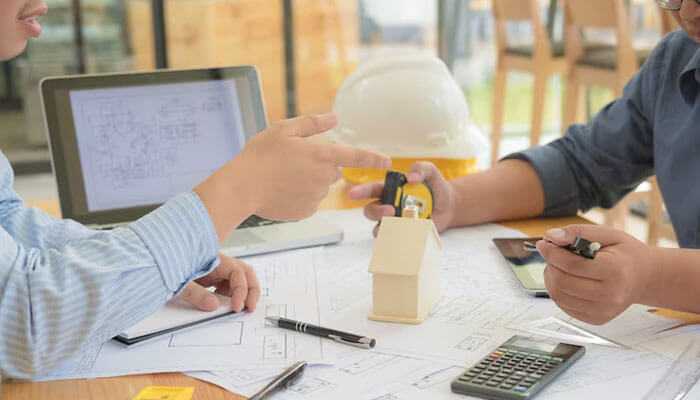 Two people going over blueprints, model house, and calculator-both of which represent the needs of construction companies cash flow.