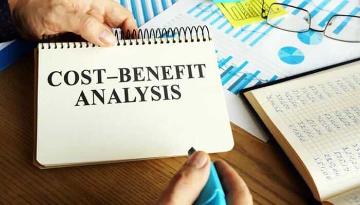 A person highlighting on a notebook, where it is written cost-benefit analysis, related to bamboohr pricing are present on the desk.