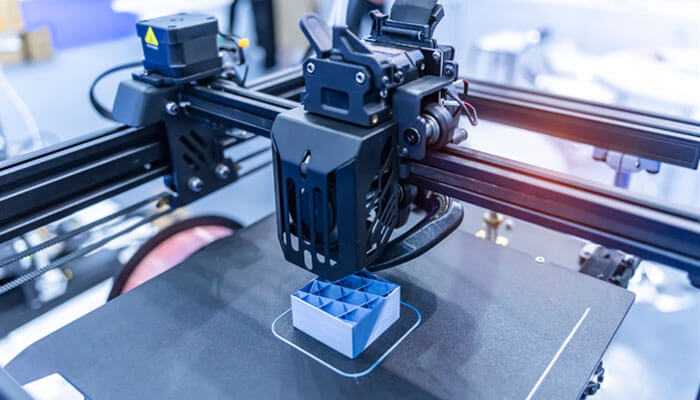 Close-up of a 3d printer in light industry, building a small, blue and white grid-patterned object, demonstrating additive manufacturing.