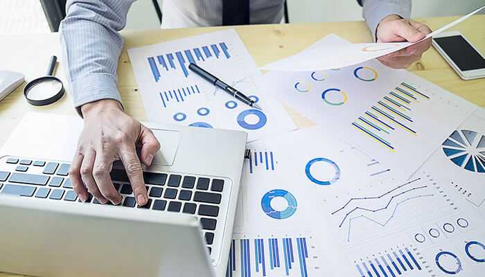 Businessperson analyzing data charts and graphs on paper and using a laptop, representing data analysis and strategic planning for app development services