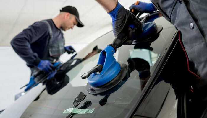 Two technicians using suction tools to install or repair a car windshield, illustrating windshield repair costs in burlington.