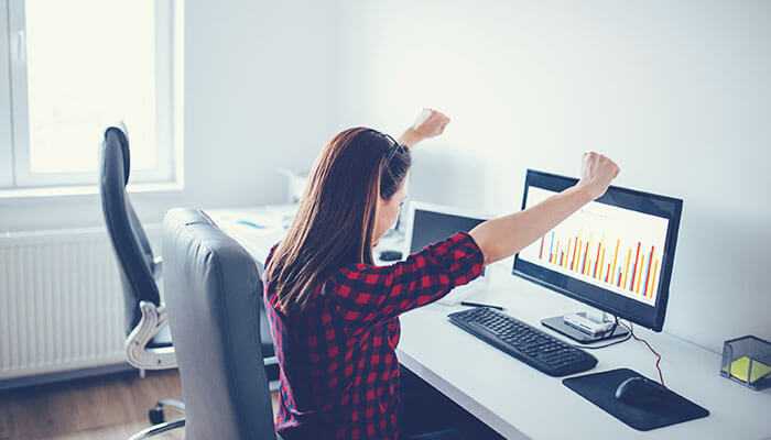 Women in hedge funds as a woman celebrates success at her desk, viewing a positive chart on her computer, signifying achievement and progress in finance or data analysis.