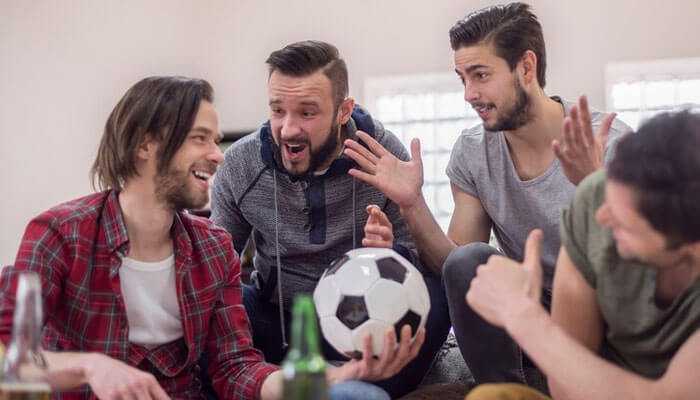 A group of friends enthusiastically discussing a soccer game while holding a ball symbolizes sports wagering with friends.