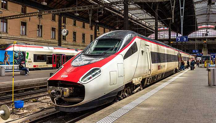 A modern high-speed train at a station platform, with passengers nearby and a covered terminal structure in the background, perfect for first-time travelers to france