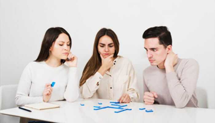 Three men at the table, brooding and intent, consider the jigsaw pieces, a metaphor for problem-solving and collaboration.