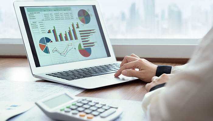 A person analyzes employee benefits data charts on a laptop with a calculator nearby