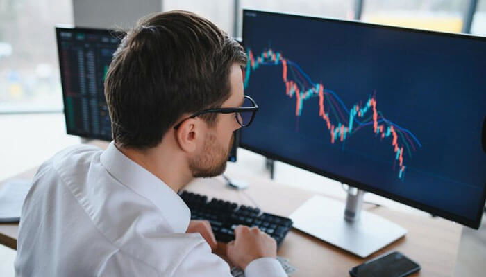 Various monitors with candlestick charts showing stock market data being analyzed by a man to study the trends for investment decisions.