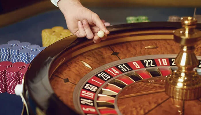 Close-up of a roulette table representing australian online casinos with a hand holding a ball about to drop onto the wheel.