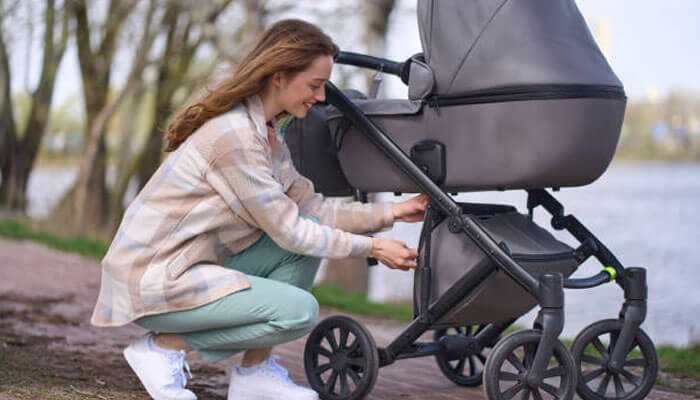 Mother adjusting a storage compartment on a high quality baby stroller while going out for an outdoor stroll.