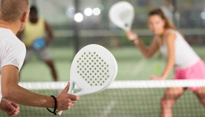 Players in a game of padel racket with a paddle in their hands ready to return the ball over the net.