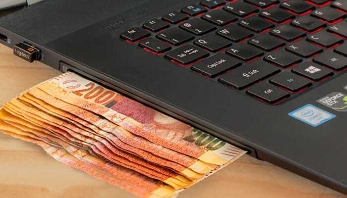 A stack of currency notes partially tucked under the keyboard of a laptop-a representation of soccer betting online.