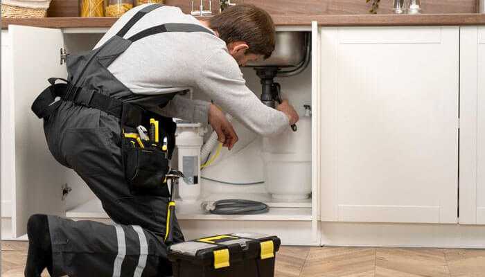 Commercial plumbers in san diego repairing plumbing under a kitchen sink with tools and a black and yellow toolbox nearby