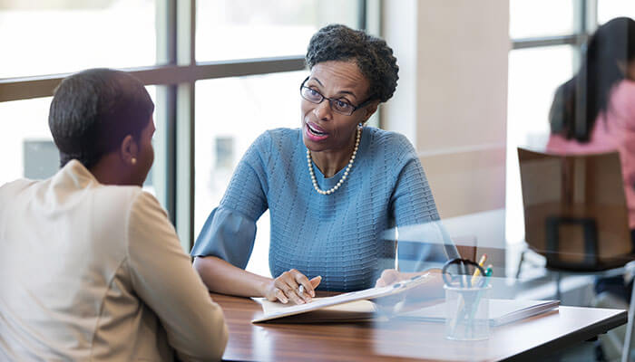 Personal loan approval two women engaged in a professional discussion at a desk in a modern office, representing collaboration or financial consultation