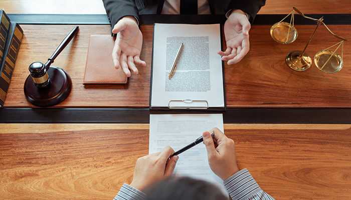 Defense against fraud allegations with a lawyer and client discussing legal documents with a gavel and scales of justice on the desk