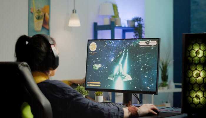 Person with headphones on playing a space video game on a desktop, showing the rise of ai powered gaming laptops.