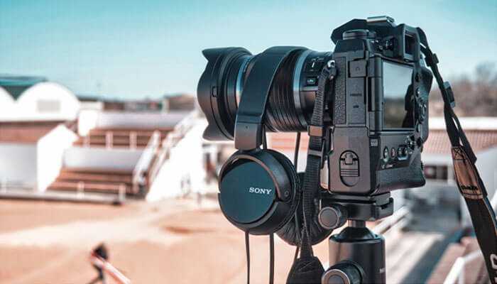 A professional camera on a tripod with sony headphones, set up outdoors, representing a video production company