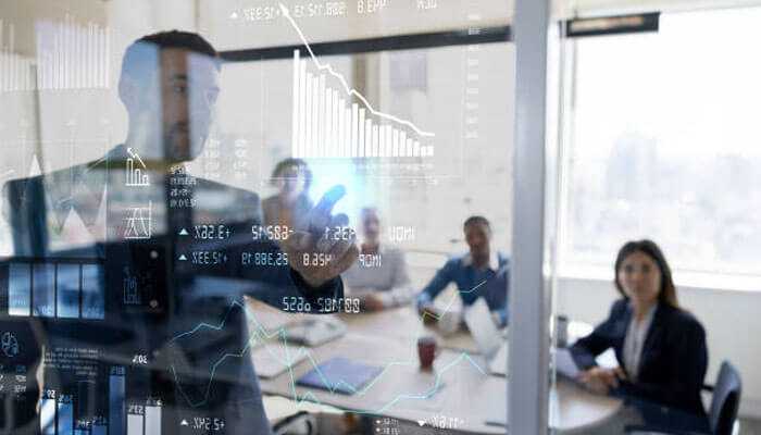 A business person demonstrating financial data on a clear screen to a team representative for companies offering investment training.