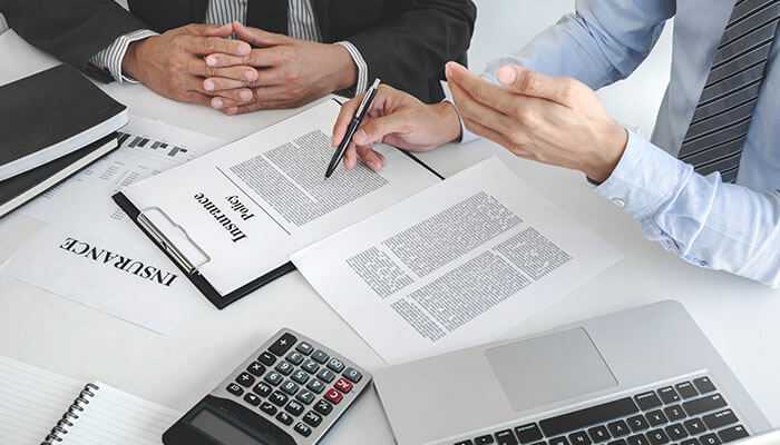 Us health insurance business professionals reviewing insurance policy documents at a desk with a laptop calculator and paperwork in a formal office setting