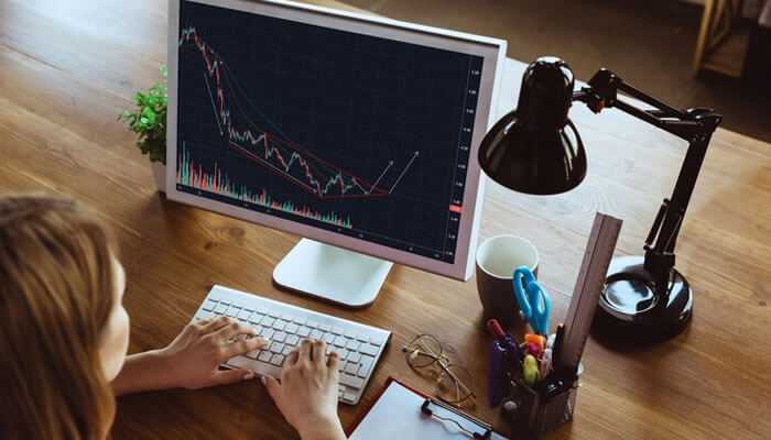 Stock market education firms: a person trading on laptop with lamp, spects, pad, pen stand on the table.