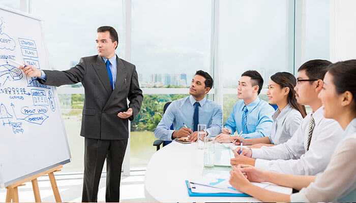 A business meeting where a man presents hos regulations on a whiteboard to a group of attentive professionals