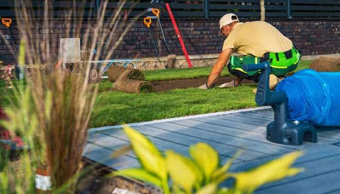 Landscaping business worker laying fresh sod on a lawn with landscaping tools in the background, emphasizing outdoor landscaping and maintenance work.