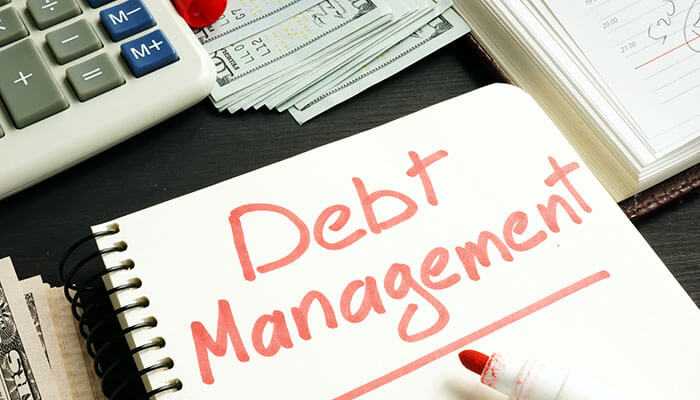 A notebook with debt management written in bold red letters, surrounded by a calculator, money, and documents, symbolizing fintech solutions for financial planning and control