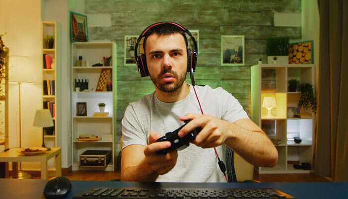 A man with a gaming headset holding a controller, playing games like html5 slot machines in a cozy room setup.