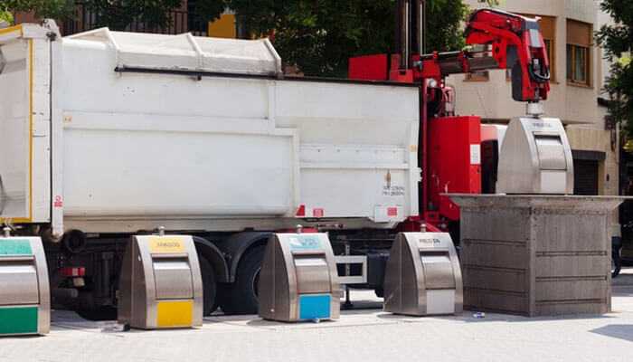 A garbage truck collects garbage from underground bins with recycling containers, leasing commercial waste equipment.