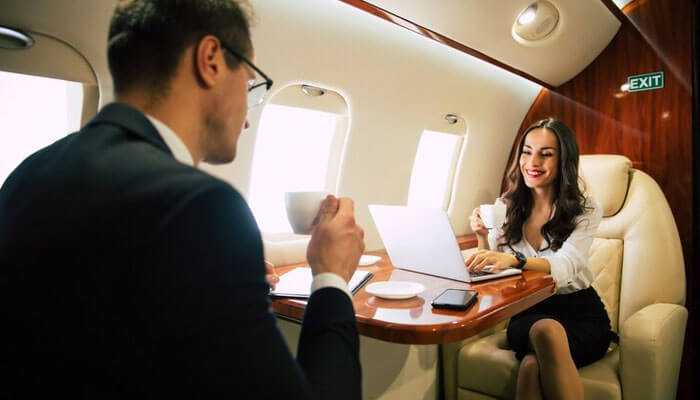 Business professionals discussing and enjoying coffee onboard corporate jet charters, with a laptop and mobile phone on the table.