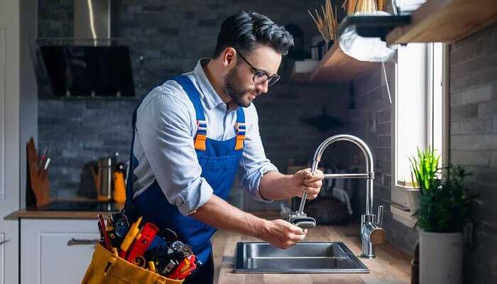 Emergency plumber in san diego fixing a faucet in a modern kitchen with wooden countertops and natural light