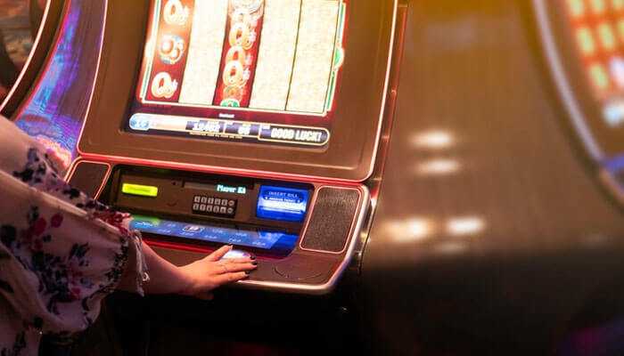 A person playing on a casino slot machine with colorful screens and bright lighting, focusing on his hand touching the buttons.