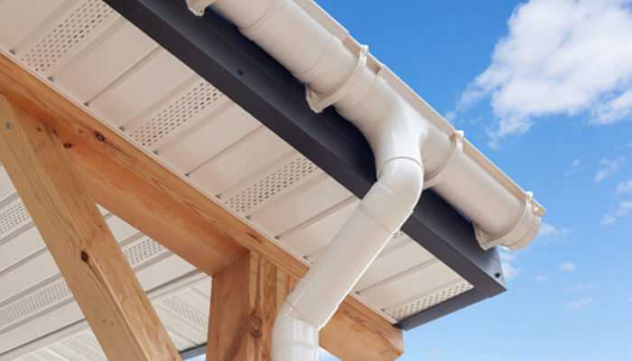 White pvc rain gutter system on the wooden structure, with the blue sky showing through.