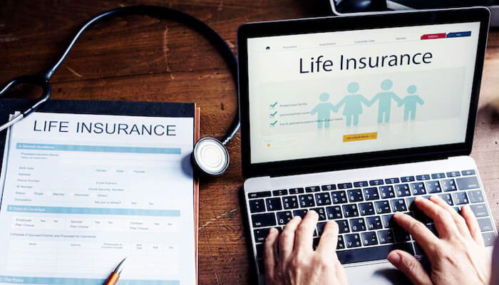 This is an image of a laptop with a life insurance webpage, an insurance form, and a stethoscope, representing insurance management.