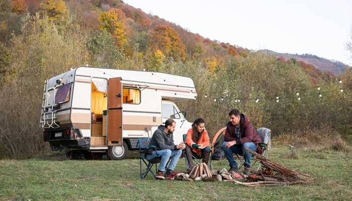 Friends having fun around a campfire near their caravan in autumn, made possible by caravan finance in australia.