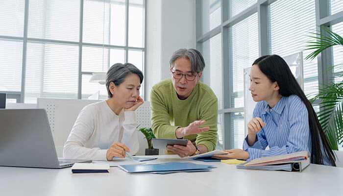 Three colleagues working in a contemporary office, discussing cybersecurity strategies while reviewing documents and using a tablet.