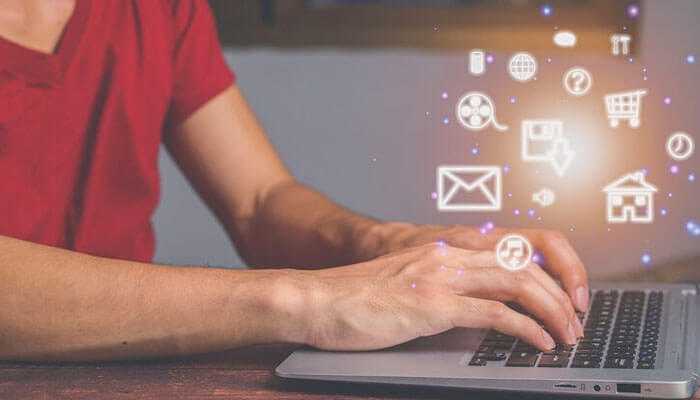 A person in a red shirt is typing on a laptop, with glowing digital icons like an email, shopping cart, and house floating above, symbolizing various online activities, ideal for small business owners.