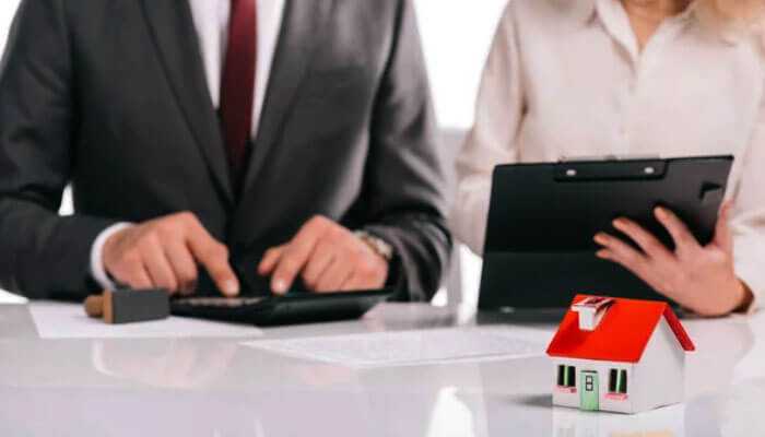 Mortgage broker for your property purchase: a model house on a table with professionals discussing mortgage options.