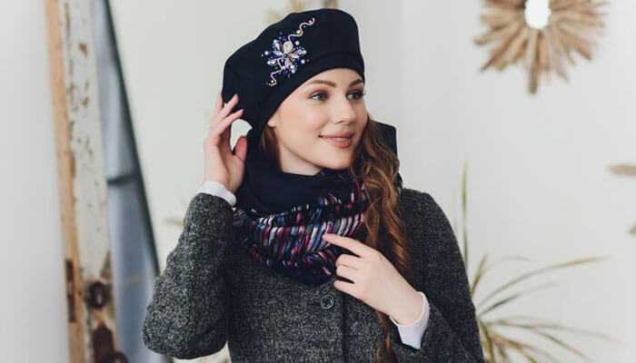 Fashionable woman in a black beret with embellishments, luxury cashmere scarf, and textured coat inside.