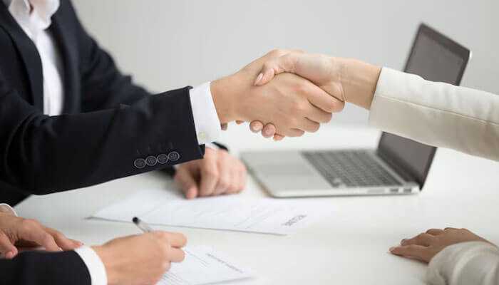 Two professionals shaking hands over a contract, a representation of partnership and collaboration during the hiring process for reactjs developers.