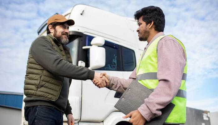 A truck driver and a logistics worker shaking hands by a truck, symbolizing freight factoring for trucking success.