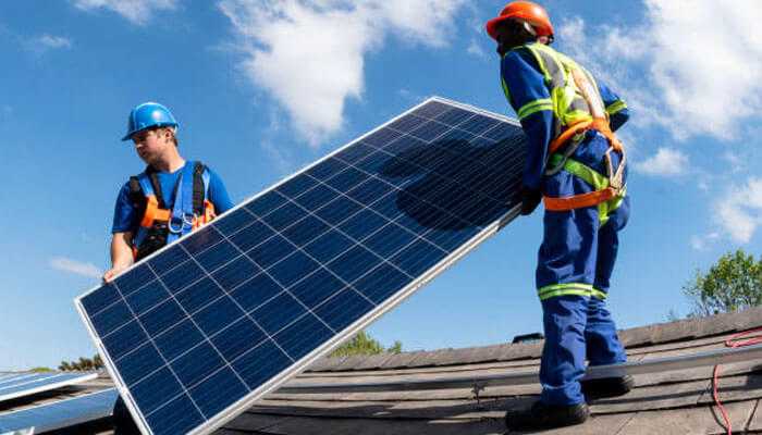 Two workers in safety gear installing solar panels on a roof, showcasing advancements in home building technology for energy efficiency.