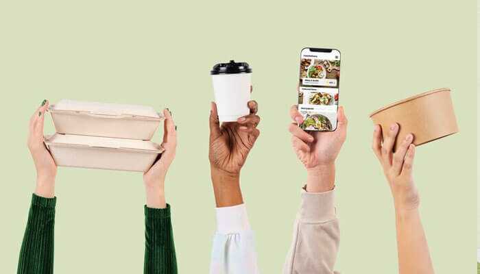 Hands holding compostable bakery packaging, a reusable coffee cup, and a phone promoting food with an app.